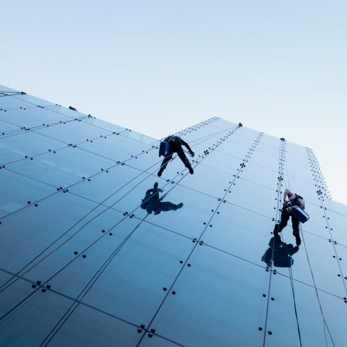 A low angle shot of two persons rappelling at the side of a tall building